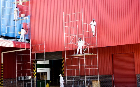 A team of industrial painters on scaffolding painting a roof facade.
